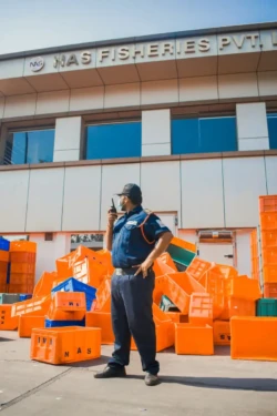 Reliable security supervision by an ABS Force professional guard at an industrial site in Kerala. A professional ABS Force security guard actively monitoring an industrial facility with a walkie-talkie, ensuring disciplined safety and asset protection. ABS Force Security Services offers expert security solutions for factories, commercial properties, residential complexes, and industrial sites across Kerala, supported by trained guards, modern systems, and dependable service. Learn more at ABSForce.in.